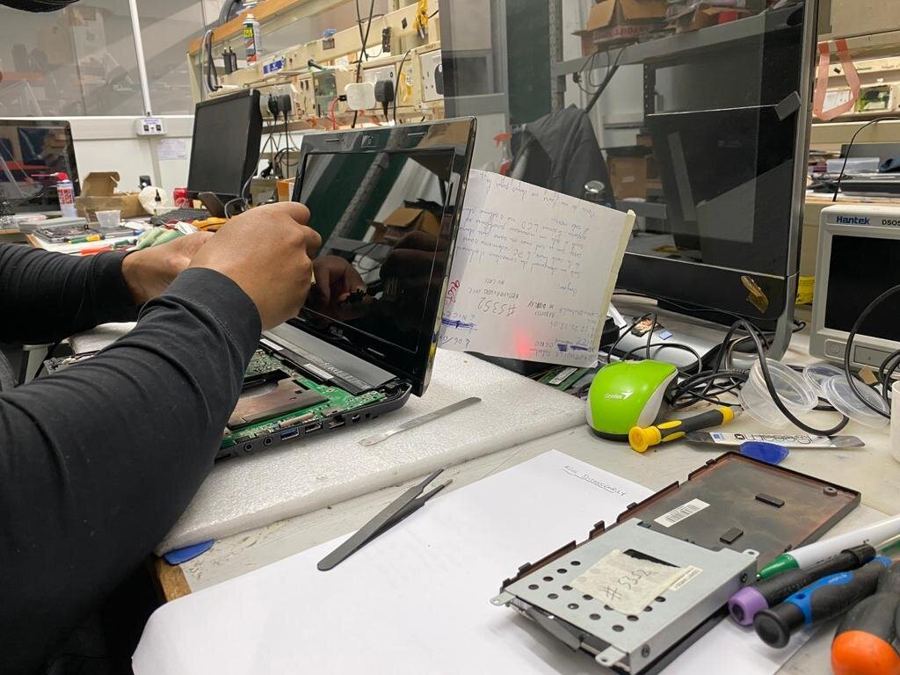 A technician working on a stripped-down laptop at the workshop bench