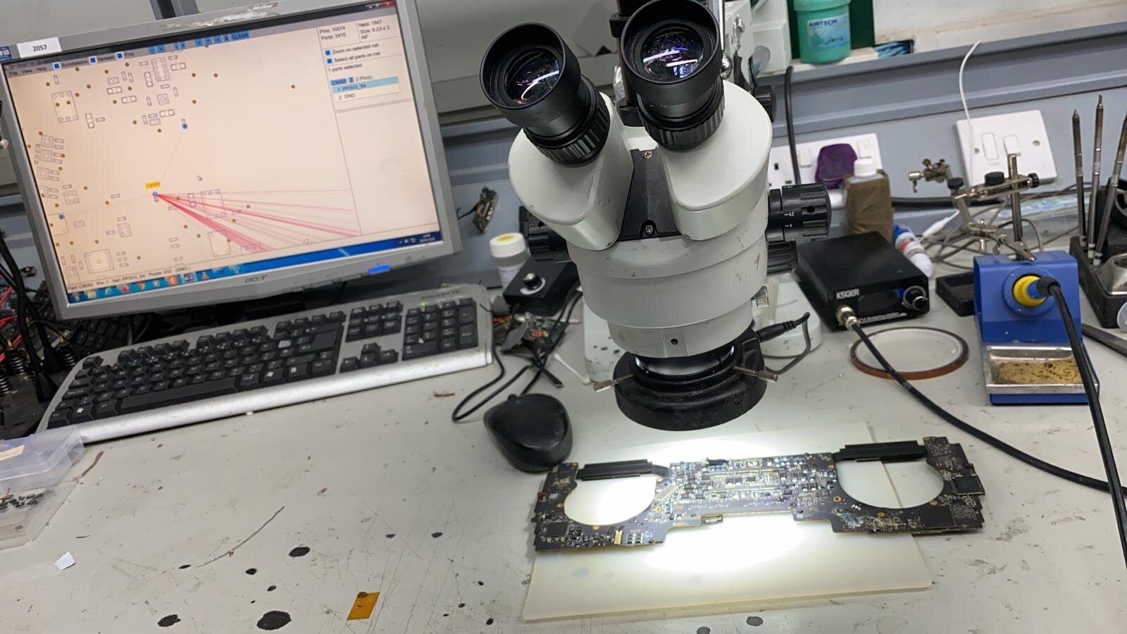 A laptop motherboard under a microscope beside a soldering station